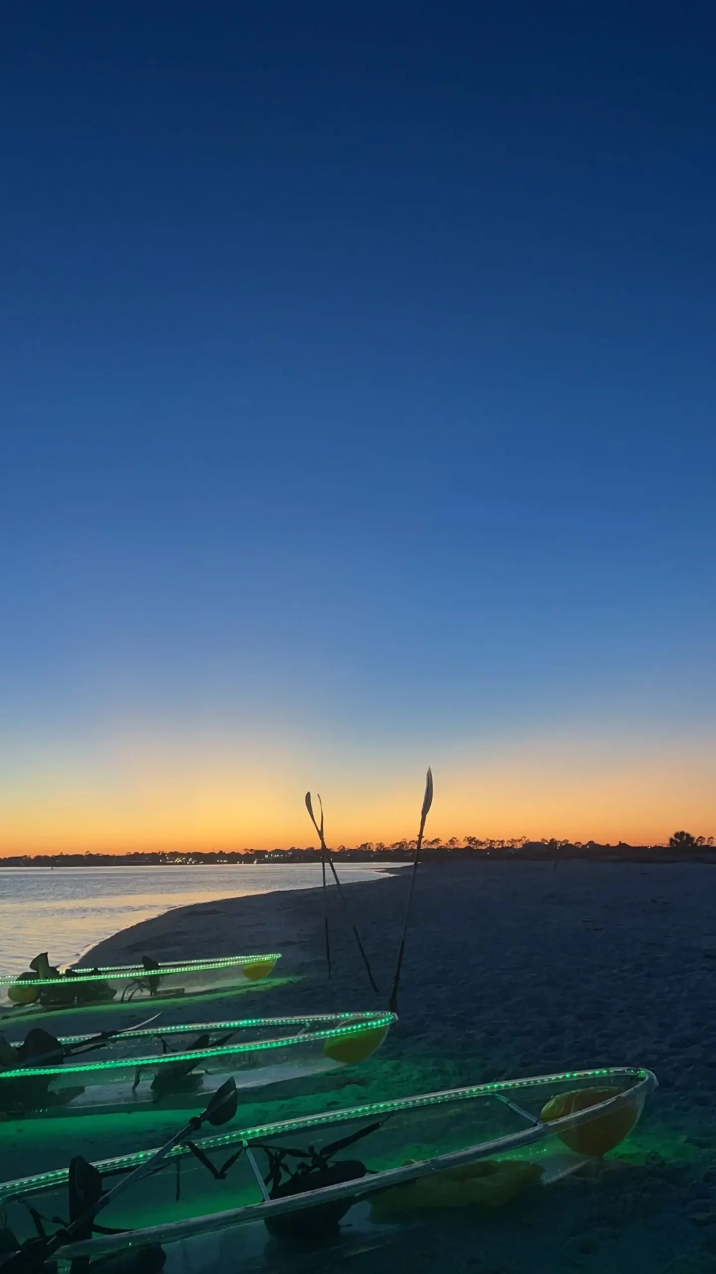 A guest paddling a neon-lit clear kayak at dusk near Orange Beach